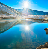 Sunrise over a serene winter lake with snow-capped mountains, highlighting the importance of UV protection; a person wearing UV Skinz UPF clothing stands at the lakeshore, emphasizing sun safety in winter activities.