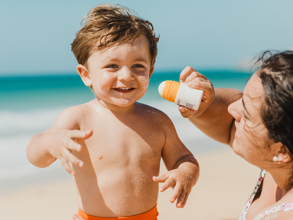 Family sun safety in action: A loving mother wearing UV Skinz beachwear protects her infant son from potential sun damage by carefully applying protective sunscreen during their beach day